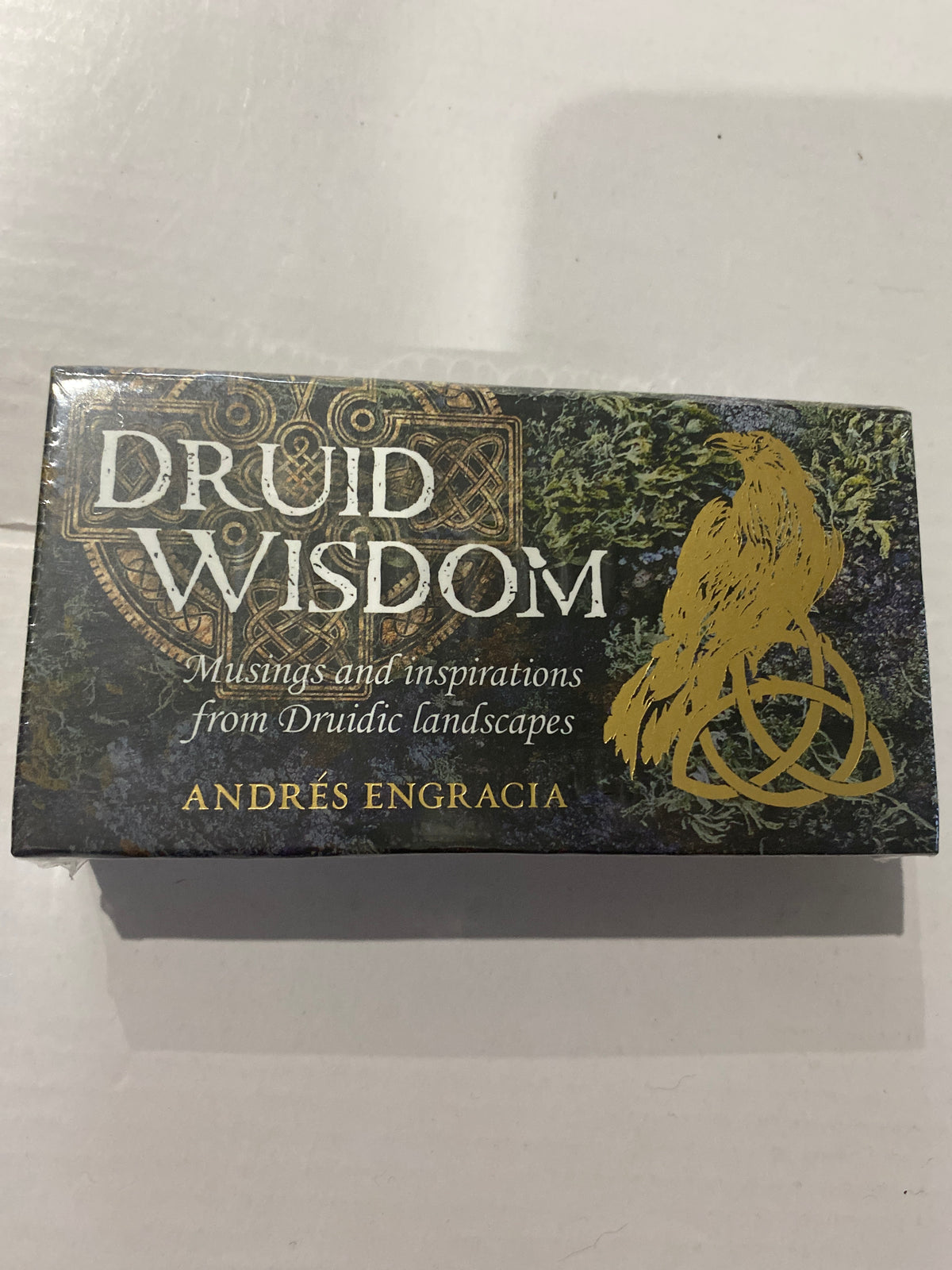 A boxed product titled "Druid Wisdom" by Andrés Engracia, shown on a plain light background. The box is dark with ornate gold and green artwork, including a raven over a triquetra symbol.
