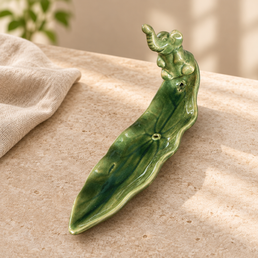 Green glazed ceramic elephant incense burner with leaf-shaped tray on a light stone tabletop